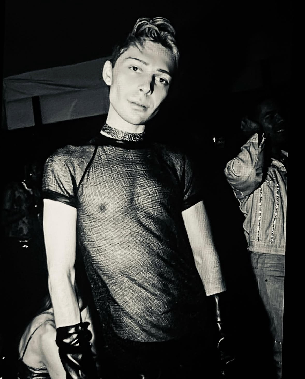 Black-and-white image of Justin Grant in a sheer mesh tank at a queer nightlife event.